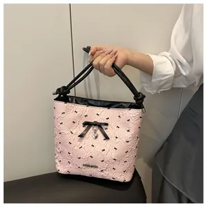 Pink textured bucket bag with black bow details and a silver heart-shaped pendant