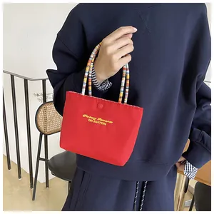 Detail of red tote bag with yellow embroidery and colorful beaded handle with button closure