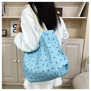 Detail of blue tote bag with black bow pattern and woven rope shoulder strap texture