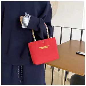 Detail of red canvas handbag with colorful textured handle and snap closure shown in use
