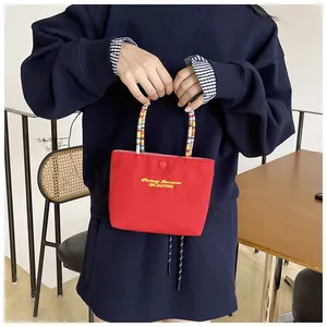 Detail of red canvas handbag with yellow embroidery and colorful beaded chain handle