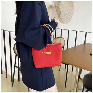 Detail of red canvas tote bag featuring yellow embroidery and colorful beaded handle