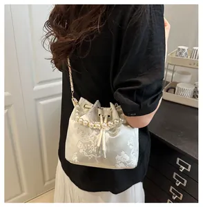 Detail of floral embroidery on ivory satin bucket bag with pearl handle and metal chain