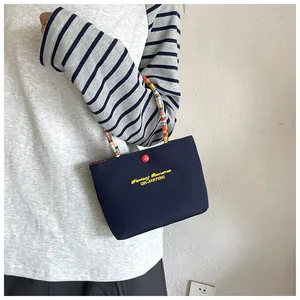 Detail of navy handbag with yellow text, red snap closure, and colorful woven handles