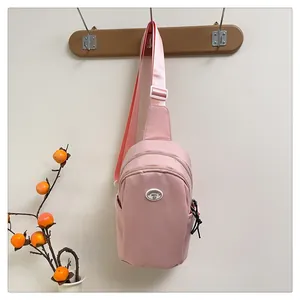 Close-up of pink crossbody bag with logo badge and adjustable wide strap on wooden hook