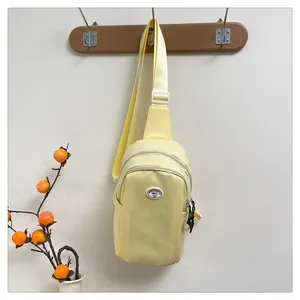 Detail of light yellow nylon chest bag with oval logo and dual zipper compartments