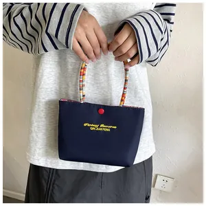Detail of navy blue handbag featuring yellow embroidery and colorful braided handle