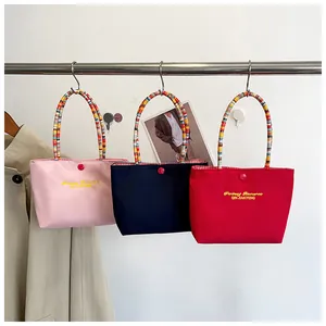 Detail of embroidered mini canvas handbags with rainbow woven handles and striped lining