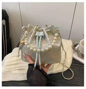 Detailed view of embroidery silk bucket bag with pearl handle and golden floral patterns