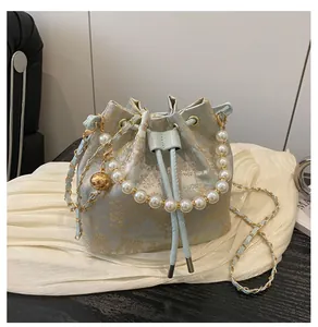 Detailed close-up of light blue silk bucket bag with gold floral embroidery and pearl handle