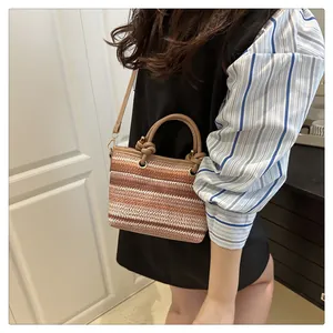 Detail of striped straw handbag with brown leather strap and gold metal hardware