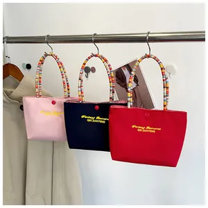 Detail of colorful canvas handbags featuring yellow embroidery and rainbow striped handles