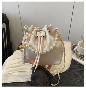 Detail view of cream bucket bag featuring floral embroidery and elegant pearl handle