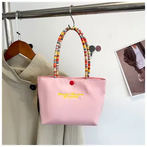 Pink canvas tote bag featuring colorful woven handles and yellow fantasy embroidery detail