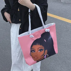 Pink canvas tote bag with black woman illustration and white rope handles shown outdoors