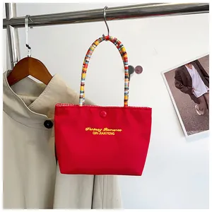 Detail of red canvas tote with yellow embroidery, drawstring handle and plaid lining