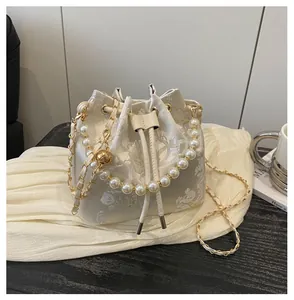 Detailed embroidery and pearl handle chain on cream-white satin bucket bag