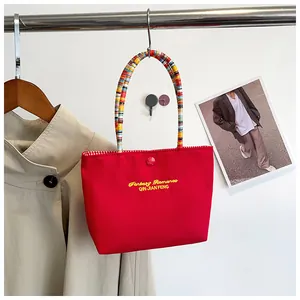 Detail of red canvas handbag with colorful woven handles and plaid lining texture