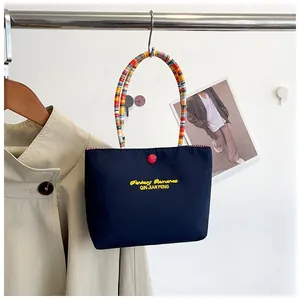 Detail of navy blue canvas tote bag featuring yellow embroidery and colorful woven handle