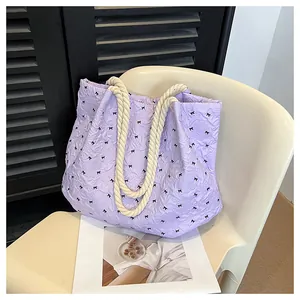 Detail of purple quilted tote bag with black bow patterns and cream rope handles
