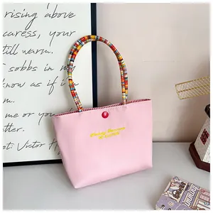 Detail of pink embroidered tote bag with colorful braided handle and red button accent