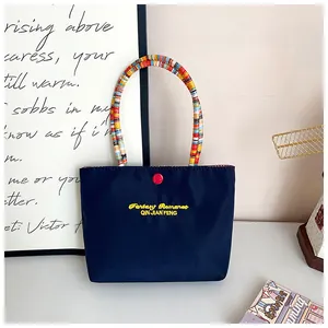 Close-up of navy blue embroidered tote bag with colorful beaded handle and yellow text
