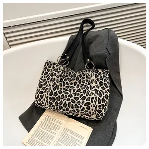 Detail of leopard print canvas tote bag with black leather handle on a grey suit jacket