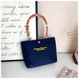 Detail of navy blue nylon handbag with vibrant rainbow beaded handle and yellow embroidery