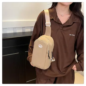 Detail of a beige crossbody chest bag featuring adjustable strap and circular logo patch