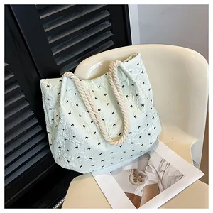 Detail of light green tote bag featuring black bow patterns and braided rope handles