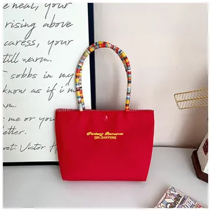 Detail of red nylon tote bag with embroidered logo and colorful beaded braided handle