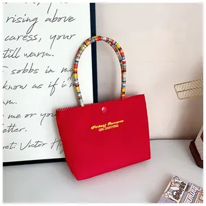 Detail of red canvas handbag featuring yellow embroidery and colorful beaded handle
