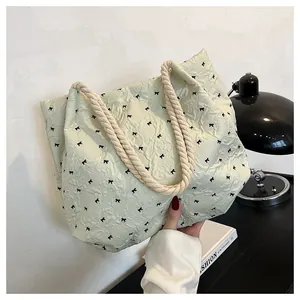Detail of light green quilted tote bag with black bows and thick cotton rope handle