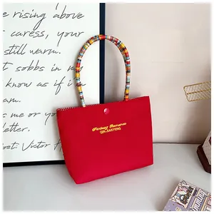 Detail of red tote bag with colorful wrapped handle and gold logo on white surface