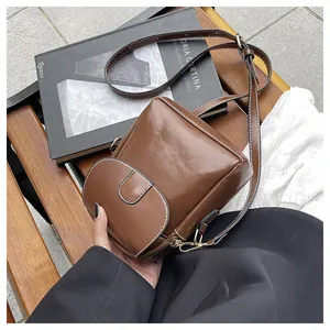 Detailed view of a brown crossbody bag with contrast stitching and golden hardware on wood