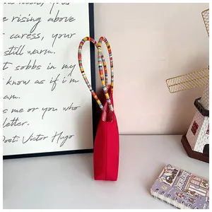 Detail of colorful braided handles on a red tote bag with striped lining and fine stitching