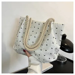 Close-up of textured cream tote bag with black bow patterns and thick rope handles