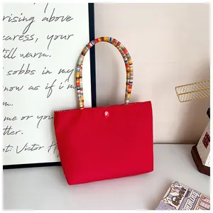 Detail of red tote bag featuring a colorful woven handle and secure button closure