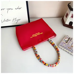 Detail of red canvas tote with gold embroidery and colorful braided handle straps