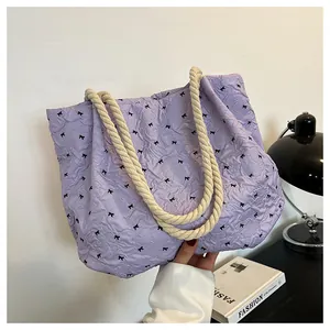 Detail of purple pleated tote bag with black bow patterns and rope handle texture