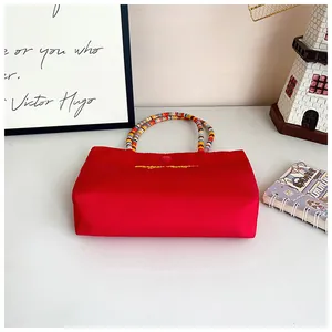Detail of red fabric handbag featuring colorful beaded handles and yellow letter embroidery