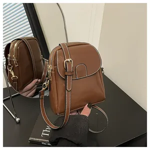Detail view showing brown leather crossbody bag with white stitching and gold hardware detail