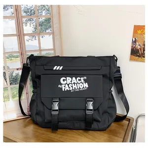 Détail du sac bandoulière en toile noire avec lettrage blanc et fermeture à double boucle