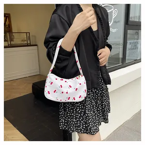 White crescent underarm bag with red cherry print and gold zipper on a fashion model