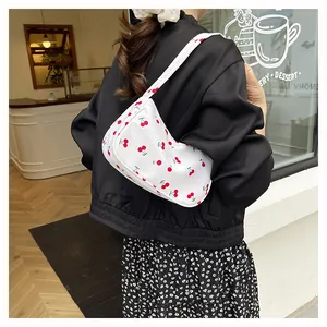 Detail of white underarm bag with red cherry prints shown in a cozy cafe setting