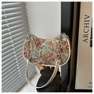 Detalle de bolso de jacquard floral con lazo plateado y correa de cadena metálica