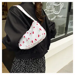 Outdoor view of a white underarm bag with cherry print on a model in a cafe setting