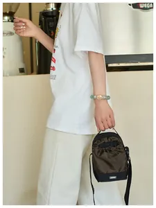 Detalle de un bolso de cubo marrón con cordón y etiqueta de moda usado por una modelo