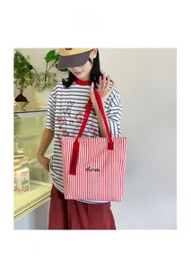 Detail of red and white striped canvas tote bag with embroidered text and handle accents