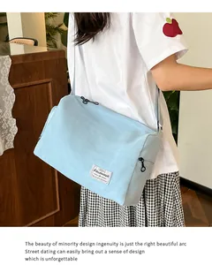 Detail of light blue canvas crossbody bag with adjustable strap and brand woven label